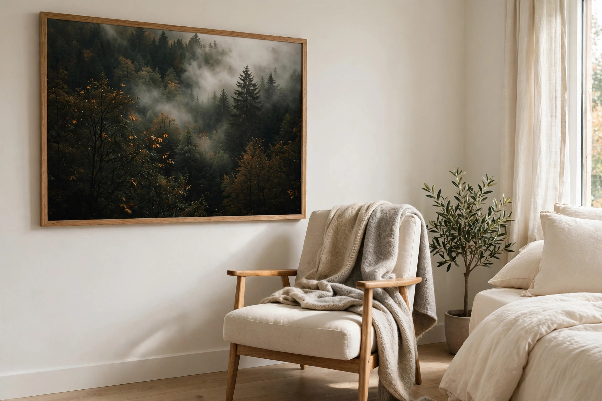 Large framed photo of a misty dark green forest above a cream reading chair with a gray blanket