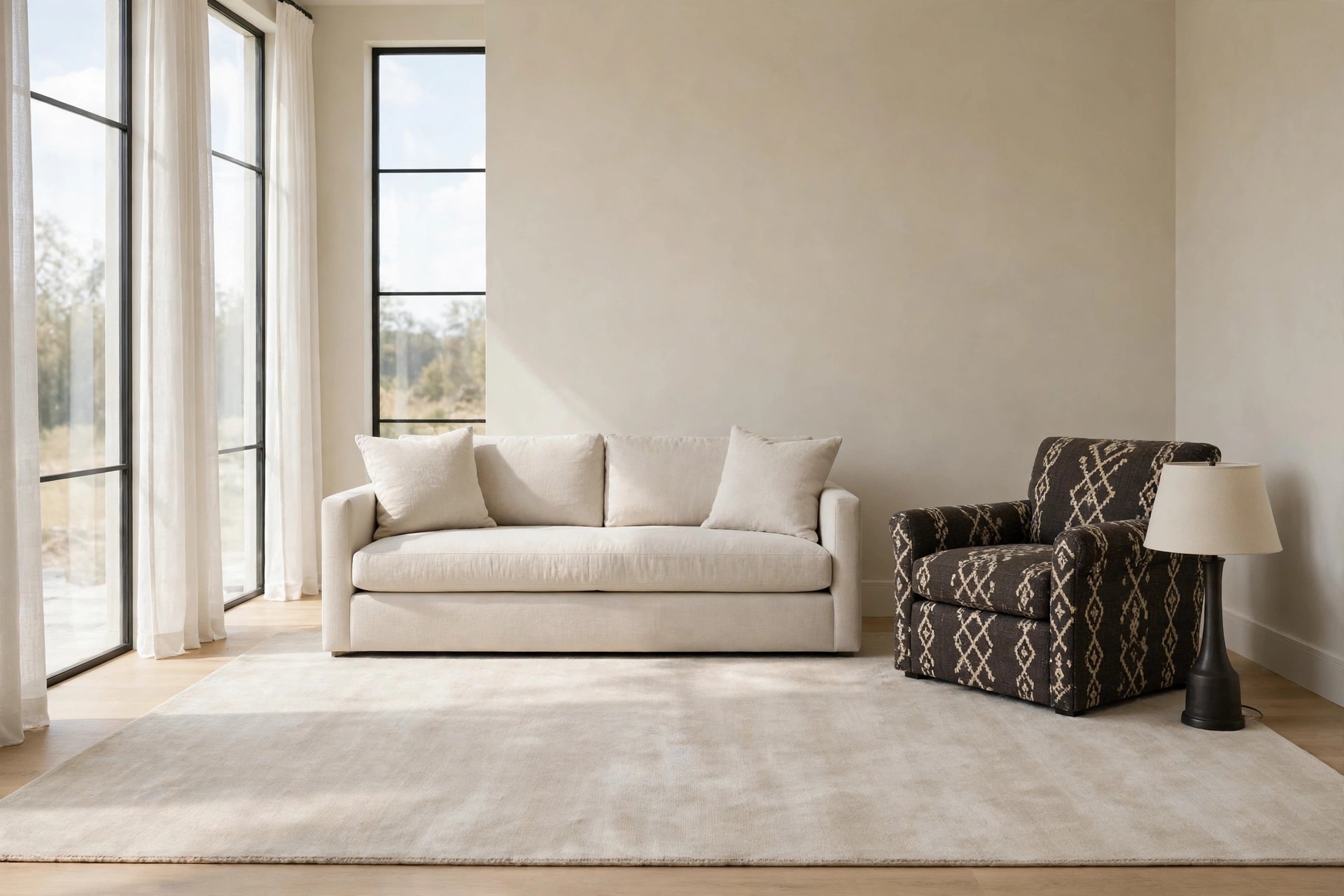 Pale beige living room with a light sofa on a pale rug and one dark charcoal armchair with a cream diamond pattern beside a dark based table lamp