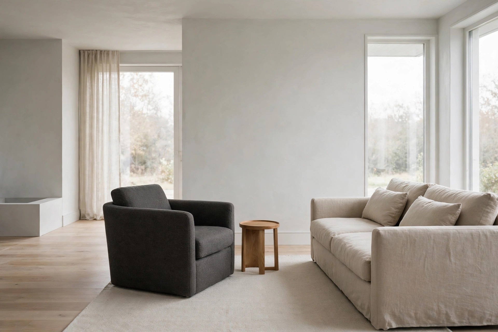 One dark charcoal grey armchair beside a beige sofa and a small round wood side table on a pale rug