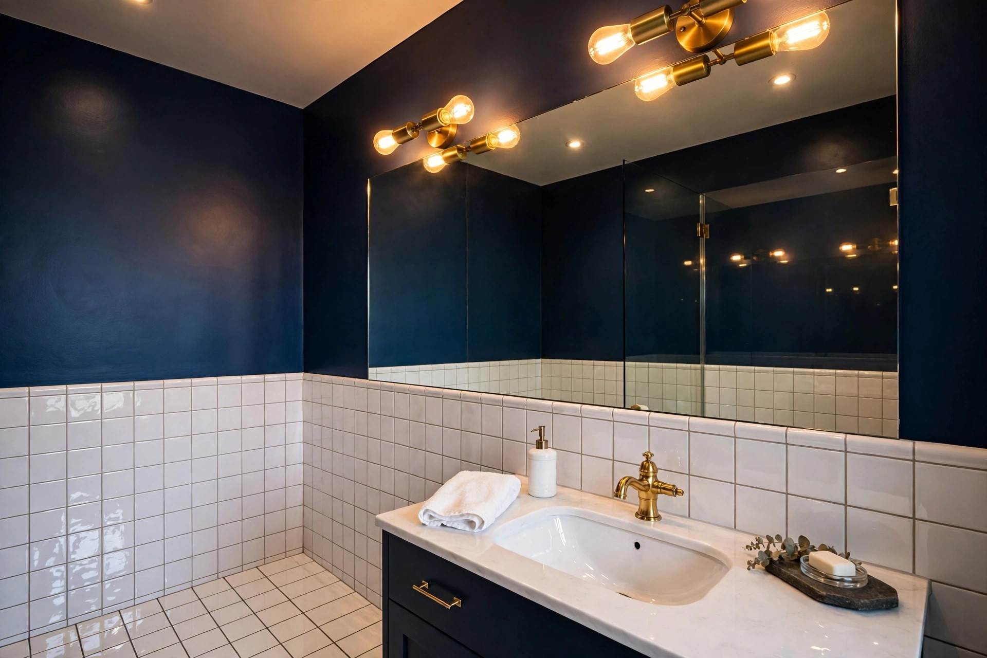 Deep navy walls creating a jewel box mood in a windowless bathroom with brass mirror lights