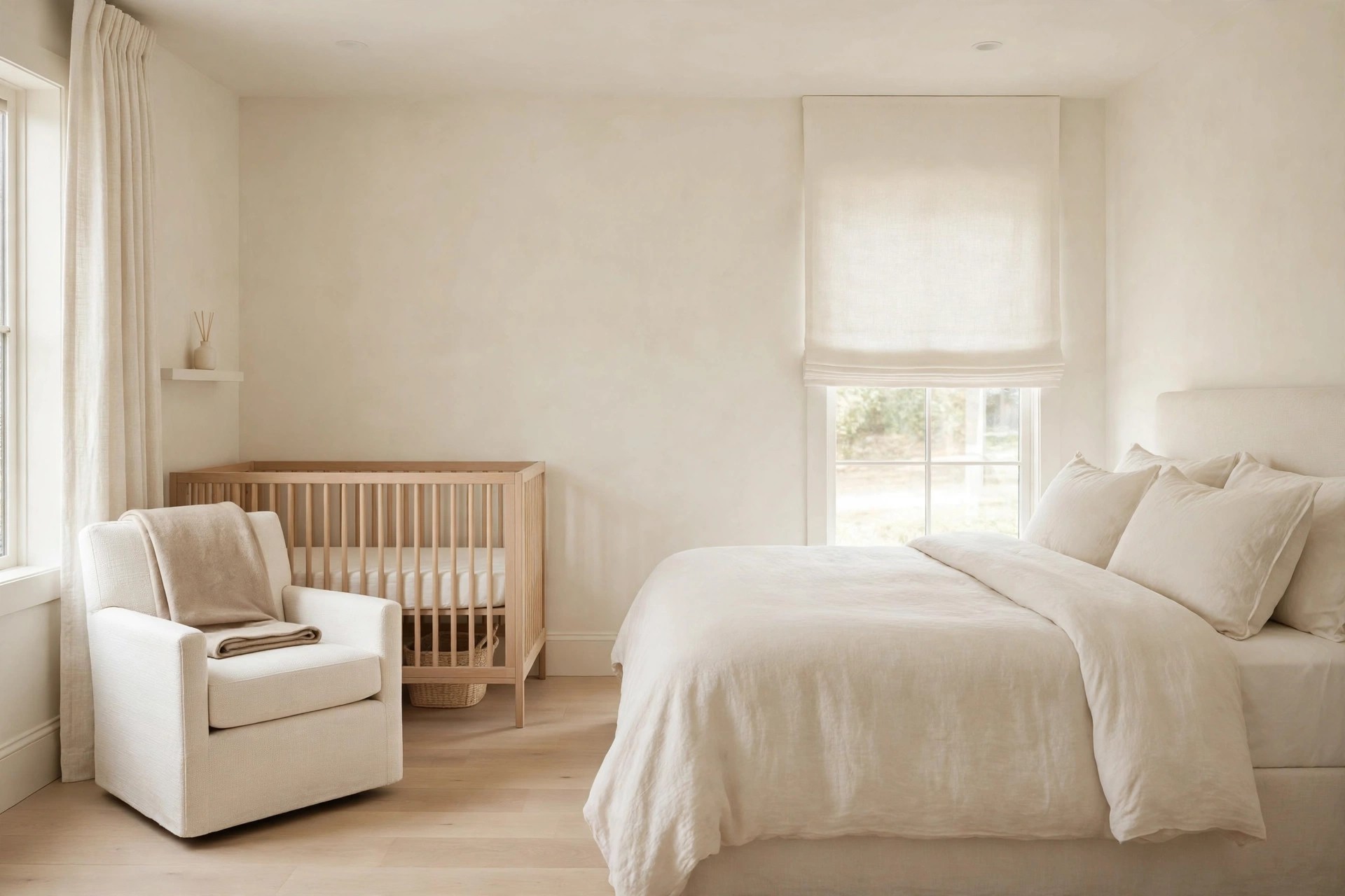 Pale cream bedroom with a cream chair holding a deeper beige throw beside a light wood crib, adult cream bed on the right