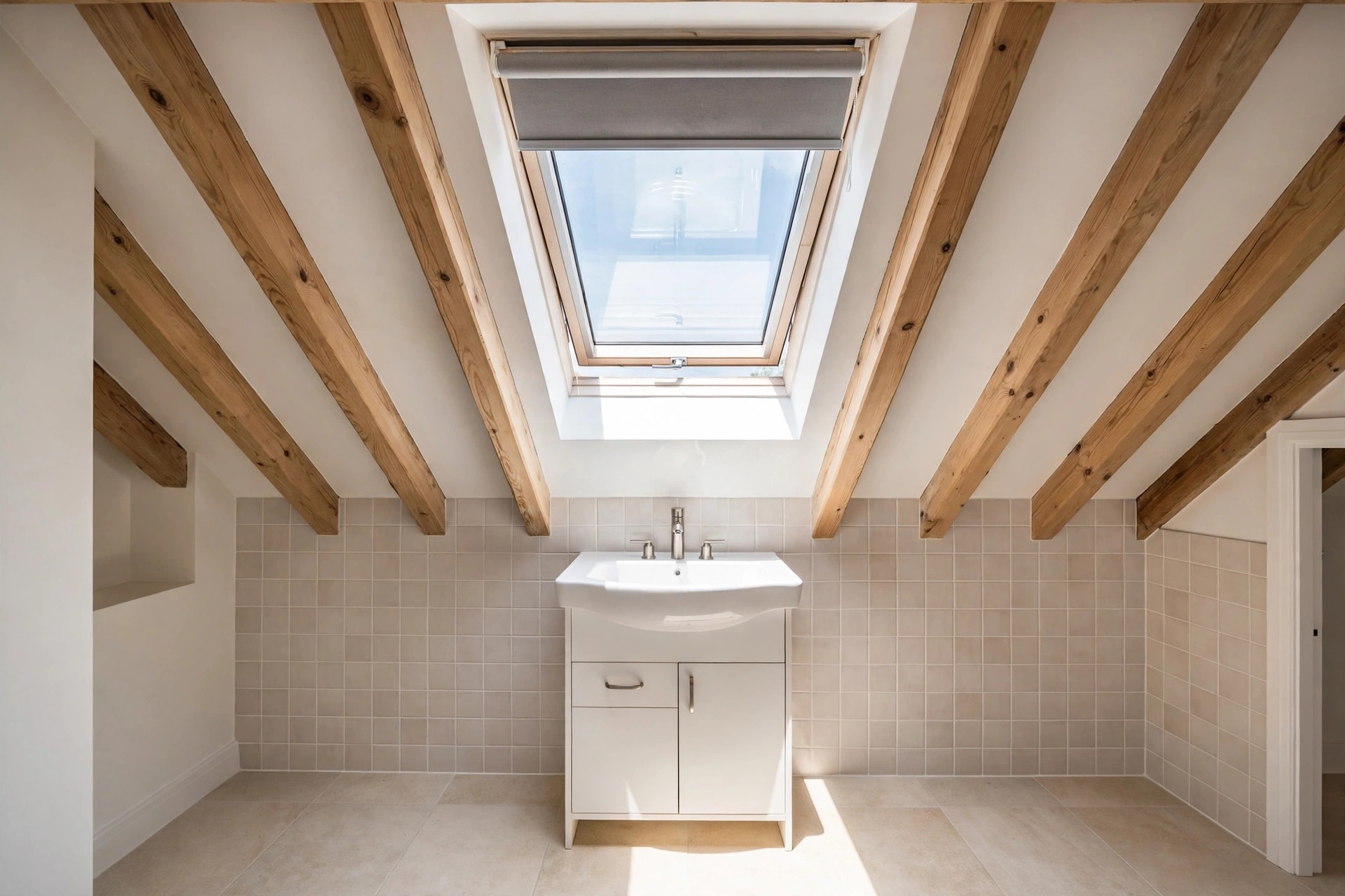 Roof window in a beamed sloped ceiling above a white sink cabinet, with light falling onto a tiled wall and floor