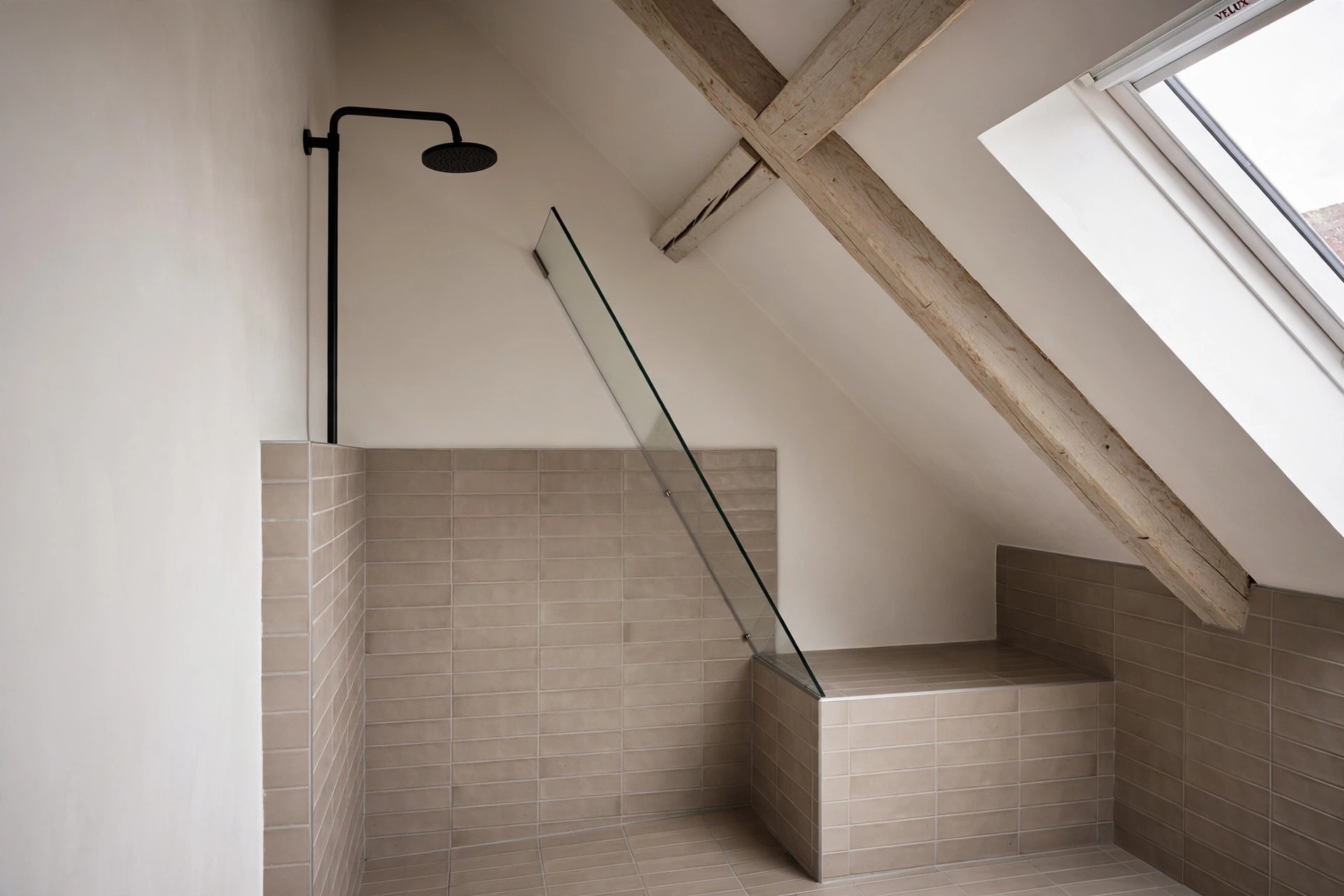 Corner shower under a slope with a shower head on the tall wall, an angled glass panel, and a tiled seat on the low side