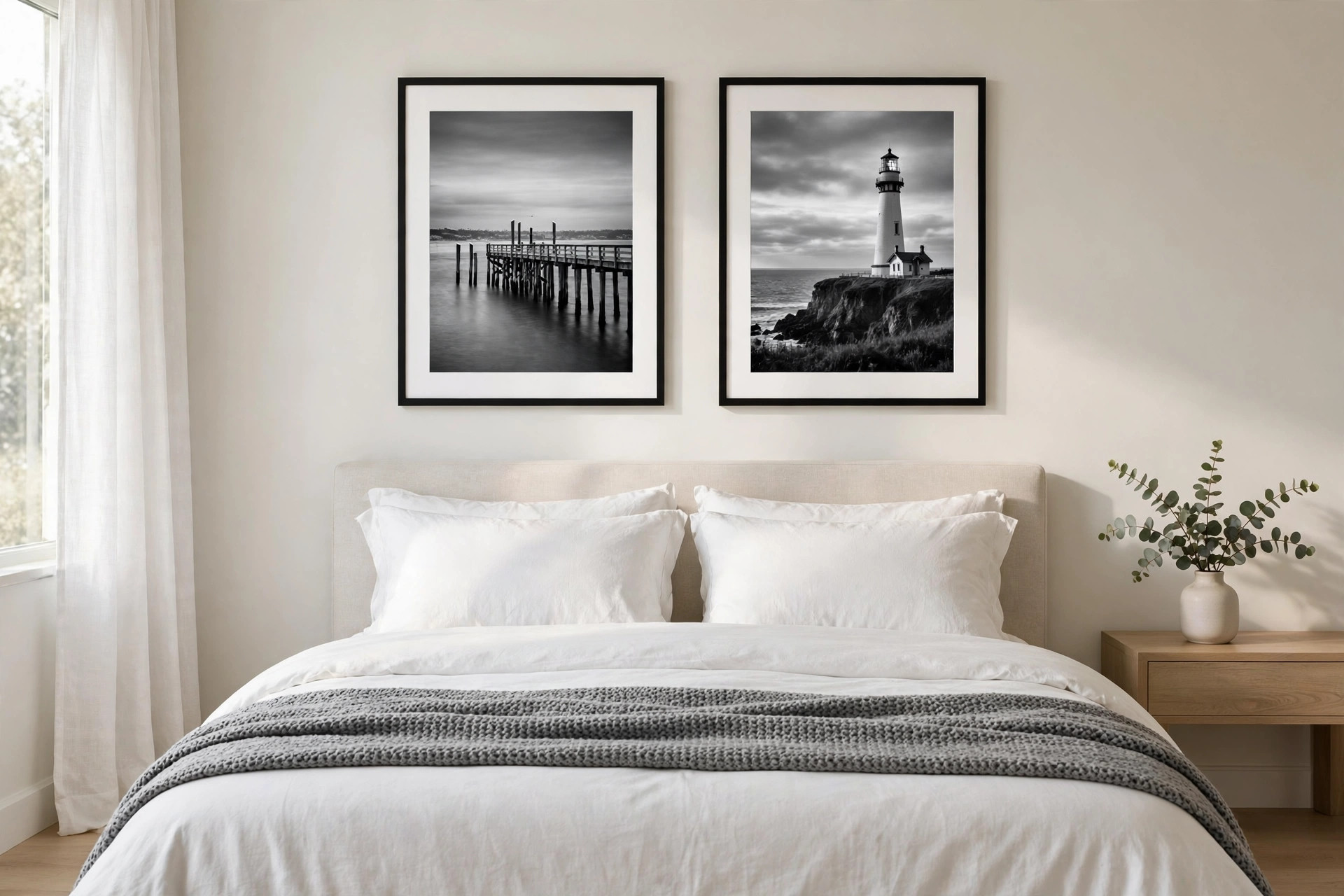 Two black and white photos, a pier and a lighthouse, in black frames above a white bed with a gray throw
